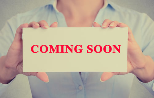 Businesswoman hands holding white card sign with coming soon text message isolated on grey wall office background. Retro instagram style image